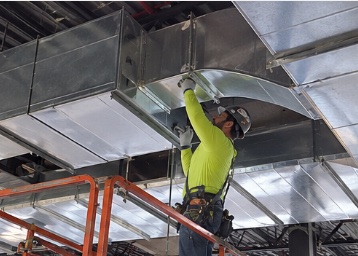 Technician installing commercial metal ductwork from an aerial lift